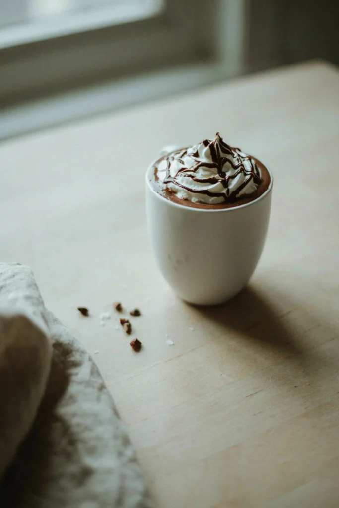 Hot cocoa topped with whipped cream and a chocolate spiderweb drizzle